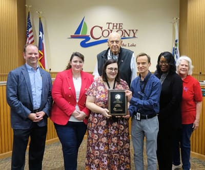 A group holding an award in front of a City of The Colony sign