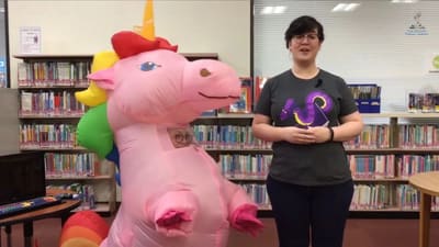 A presenter beside a giant pink unicorn plush