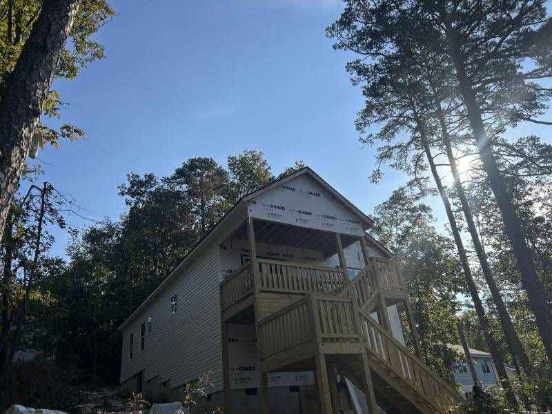 The new two-story home with a covered front deck and stairs, under tall pines