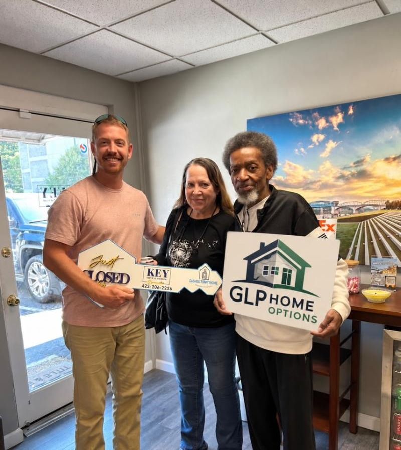 Closing day: Joey with the homeowners at the title office, holding a Just Closed key and a GLP Home Options sign