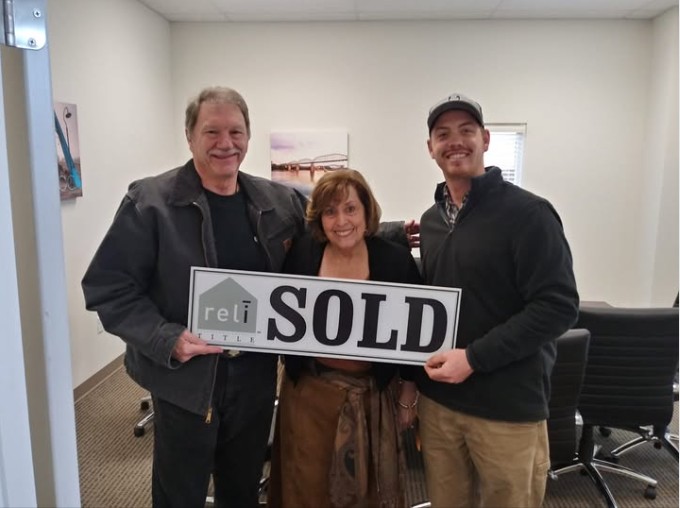 Closing day: three people smiling in an office, holding a SOLD sign