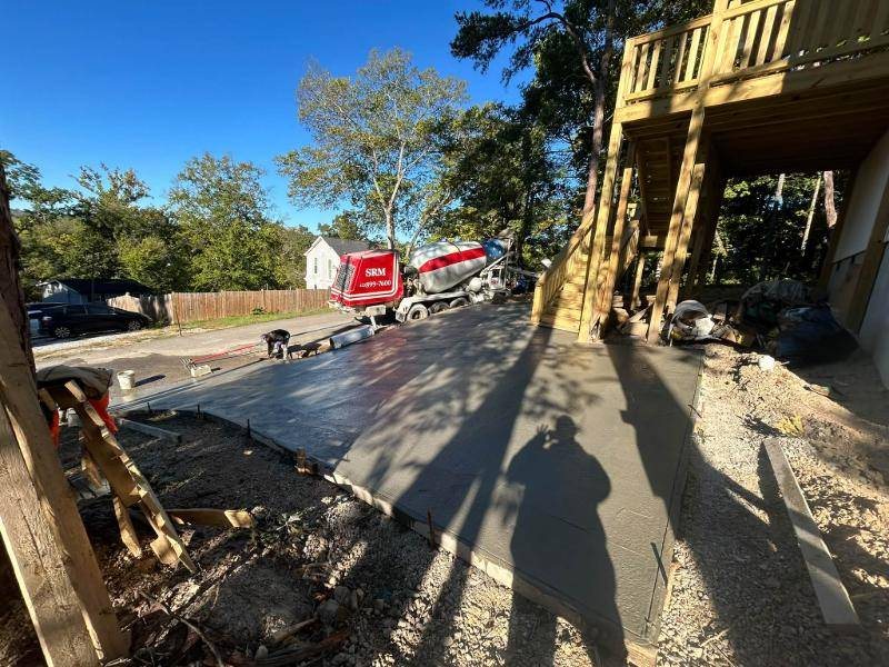 Freshly poured concrete next to a wooden deck, with a concrete mixer truck and a crew member in the background