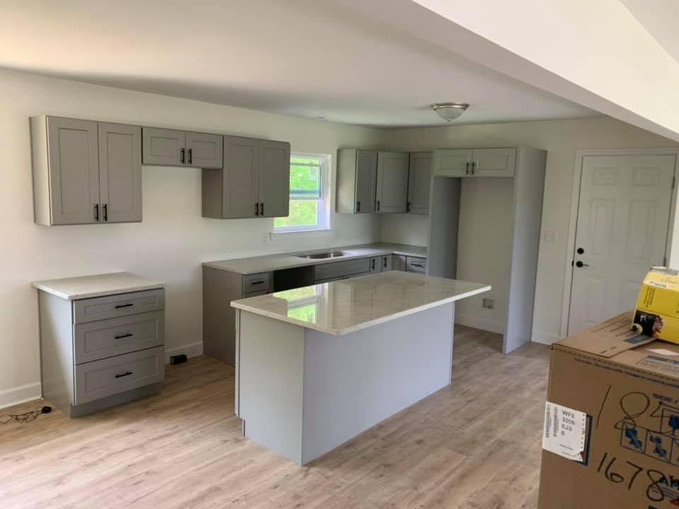 A kitchen with gray shaker cabinets, black pulls, a light countertop and a center island, with wood-look flooring.
