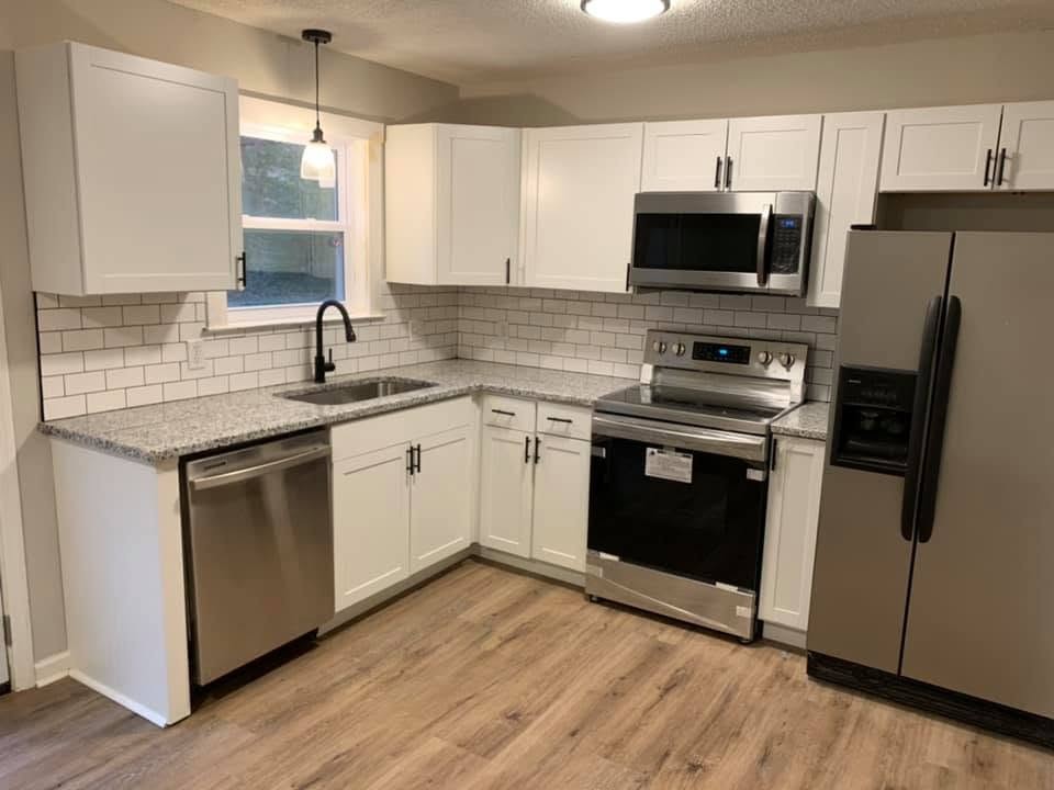 A kitchen with white shaker cabinets, white subway tile, speckled gray countertops, stainless steel appliances and wood-look flooring.