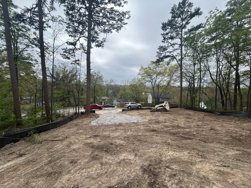 A graded lot with a gravel entrance from the street, black silt fence along the edges and a compact track loader parked at the back